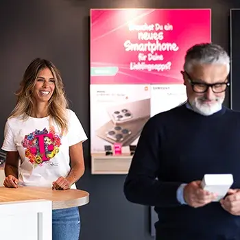 Frau am Tresen und Mann mit Smartphone vor Werbeplakat im Shop
