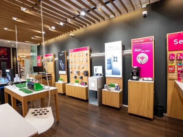 Modernes Telekom-Shop-Innenraum mit Smartphones, Zubehör und einer Kaffeebar auf Holzregalen.